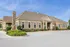 Charming, rustic-style community center with large windows and inviting entrance, surrounded by lush landscaping and sunny blue skies.