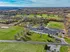 Scenic aerial view of a sprawling residential area nestled amidst lush greenery and rolling hills, showcasing a well-maintained property with ample parking and surrounded by vibrant fall foliage.