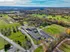 Aerial view of sprawling green landscape with a modern building complex surrounded by lush fields and vibrant autumn foliage, offering a scenic and tranquil setting.