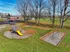 Inviting playground with vibrant yellow slide, swings, and ample green space surrounded by autumn-kissed trees, creating a perfect family-friendly environment.