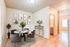 Bright dining area with chic decor features a round marble table, gray upholstered chairs, and stylish wall art. Adjacent hallway leads to bathroom and sunlit room.