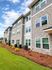 Charming apartment exterior with modern stone facade and lush landscaped surroundings under a bright blue sky.