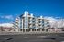 Modern apartment building with multiple balconies, set against a picturesque mountain backdrop and clear blue skies.