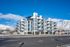 Modern multi-story apartment complex with balconies, nestled against stunning mountain views and clear blue skies.