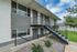 Charming multi-level apartment building with modern gray and white exterior, featuring sleek metal staircases and surrounded by lush greenery and manicured lawns.