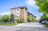 Modern apartment building surrounded by lush greenery and ample parking, set against a backdrop of clear blue skies.