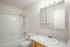 Bright and inviting bathroom featuring a modern bathtub, sleek white tiles, and a mirrored vanity with ample lighting.