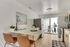 Modern kitchen with sleek countertops, stylish stools, and a well-lit dining area leading to a patio with potted plants and outdoor seating.