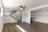 Inviting open-concept living area with modern laminate flooring, stylish ceiling fan, and adjacent kitchen. Elegant staircase leading to upper floor. Ideal for comfortable living.