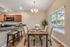 Elegant dining area with a wooden table set for six, complemented by plush upholstered chairs. The open kitchen features a sleek countertop and warm wooden cabinets, creating an inviting space for gatherings.