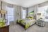 Bright and elegant bedroom featuring a plush bed with green accents, modern decor, and large windows inviting natural light.