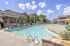 Inviting outdoor pool area with stylish lounge chairs and a shaded pergola, surrounded by beautiful brick buildings and lush greenery under a bright blue sky.