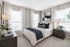 Bright and elegant bedroom featuring a plush bed with green accents, modern decor, and large windows inviting natural light.