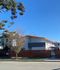 Modern apartment building with sleek design and vibrant orange accents, surrounded by greenery and a wooden fence.