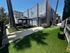 Modern apartment complex with a charming outdoor space featuring artificial grass, tall palm trees, and a stylish gazebo. Ideal for creative outdoor relaxation.