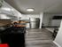 Modern kitchen with sleek stainless steel appliances, elegant white cabinetry, and rich wood flooring, leading into a cozy living area.