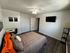 Inviting bedroom with modern decor, featuring a cozy bed with vibrant pillows, sleek wall-mounted TV, and stylish workspace under a ceiling fan.