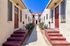 Charming Mediterranean-style apartment complex with vibrant red doors, picturesque pathway, and lush landscaping under a bright blue sky.