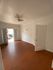 Bright, airy room with a wooden floor, elegant ceiling fan, and doors leading to a sunlit outdoor space.