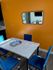 Bright dining area with vibrant orange accent wall, modern white marble table, and elegant blue velvet chairs under natural sunlight.