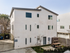Charming contemporary apartment exterior with crisp white fa&ccedil;ade, lush landscaping, and serene outdoor seating area.