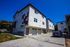 Modern apartment complex with distinctive geometric facade, featuring multiple garages and a sunlit driveway, set against a vibrant blue sky.