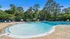 Inviting outdoor pool area with sun loungers, surrounded by lush greenery and tall trees, offering a serene retreat.