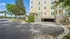 Charming yellow apartment building with stone accents, surrounded by lush greenery and palm trees, offering ample parking space.