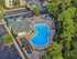 Arial view of luxurious apartment complex with a stunning resort-style pool, surrounded by lush greenery and comfortable lounge areas.