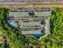 Vibrant aerial view of a luxurious apartment complex surrounded by lush greenery, featuring multiple buildings, spacious parking, and an inviting pool area.