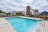 Inviting community pool area with sparkling blue water, surrounded by comfortable lounge chairs and a stylish clubhouse in the background.