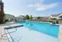 Inviting community pool area with crystal-clear water, surrounded by comfortable lounge chairs and lush landscaping under a bright blue sky.