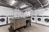 Modern apartment laundry room with multiple high-efficiency washers and dryers, sleek countertops, and stylish wood flooring.