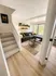 Bright, modern living room with a stylish gray sectional, accent pillows, and charming wall shelves. Features large window for natural light and tasteful decor. Inviting atmosphere with cozy carpeted stairs leading up.