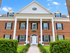 Charming brick apartment building with classic colonial architecture, featuring white pillars and lush greenery.