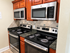 Modern kitchen featuring dual stainless steel ovens and microwaves, surrounded by elegant cherry wood cabinetry and sleek granite countertops.