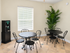 Bright, inviting community room with elegant black wrought iron tables, lush greenery, and large window for natural light.