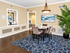 Chic dining area with elegant marble-top table, plush chairs, and ocean-themed artwork, complemented by a vibrant plant and stylish lighting.
