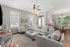 Bright and inviting living room with plush gray sofas, accented by modern decor and a stylish ceiling fan, flowing seamlessly into a cozy dining area with abundant natural light.