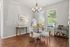 Charming dining area with elegant chandelier, cozy round table set, and a stylish bar cart. Sunlight streams through large windows, highlighting the warm wood floors.