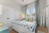 Bright and cozy bedroom featuring a plush bed with floral bedding, elegant floor-length curtains, and a stylish mirror.