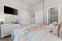Bright and cozy bedroom featuring a colorful quilt, plush bedding, modern dresser, and wall-mounted TV.
