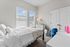 Bright and cozy bedroom with large windows, featuring a plush white bed, elegant dresser, and soft lighting for a serene atmosphere.