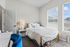Cozy bedroom with a plush bed, stylish white linens, and abundant natural light pouring through large windows.