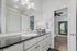 Chic bathroom with sleek black granite countertop, elegant white cabinetry, and modern lighting, leading into a cozy bedroom with a stylish mirror.