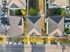 Aerial view of charming residential neighborhood showcasing three cozy homes with triangle-shaped rooftops, surrounded by lush greenery and ample parking.
