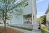 Charming light blue townhouse with inviting front porch, ceiling fan, and cozy outdoor seating, surrounded by lush greenery and a serene neighborhood setting.