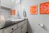 Modern bathroom with sleek black countertop, elegant faucet, vibrant orange artwork, and plush towels for a touch of luxury.