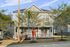 Charming two-story home with a vibrant red door, surrounded by lush greenery and a cozy front porch perfect for relaxation.