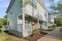 Modern two-story home with a charming front porch, vibrant red door, and lush landscaping, situated on a tree-lined street.